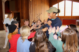 Student laughing joyfully with a group of individuals reaching hands out towards that student